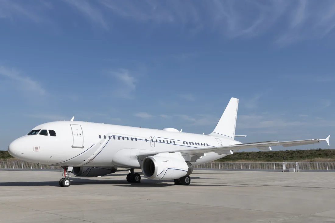 A plain white narrow-body airliner parked on an apron beneath a blue sky.
