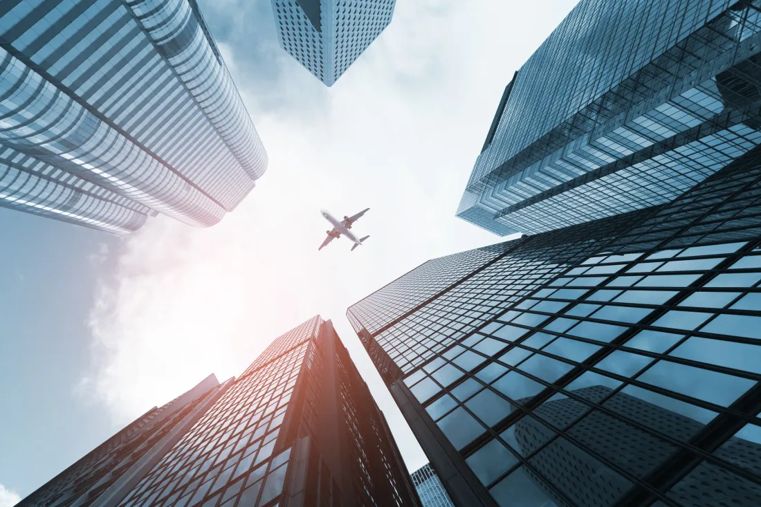 Looking straight up between glass office towers at a twin-engine airliner passing overhead.